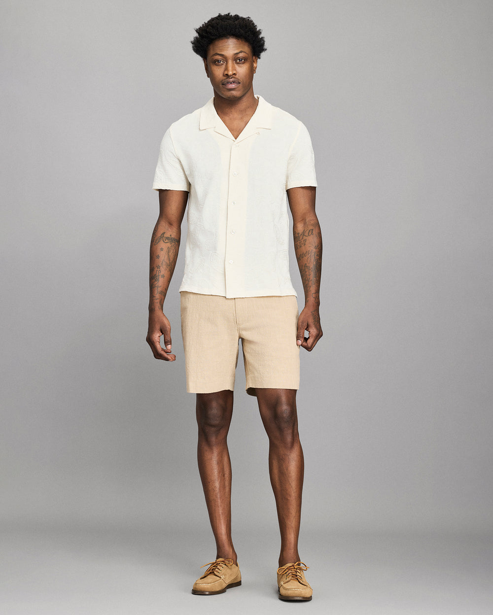 Man wearing a white shirt and beige shorts against a gray background