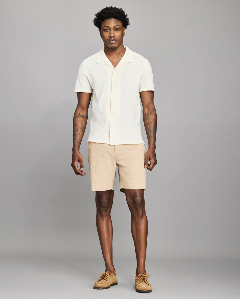 Man wearing a white shirt and beige shorts against a gray background Alternate