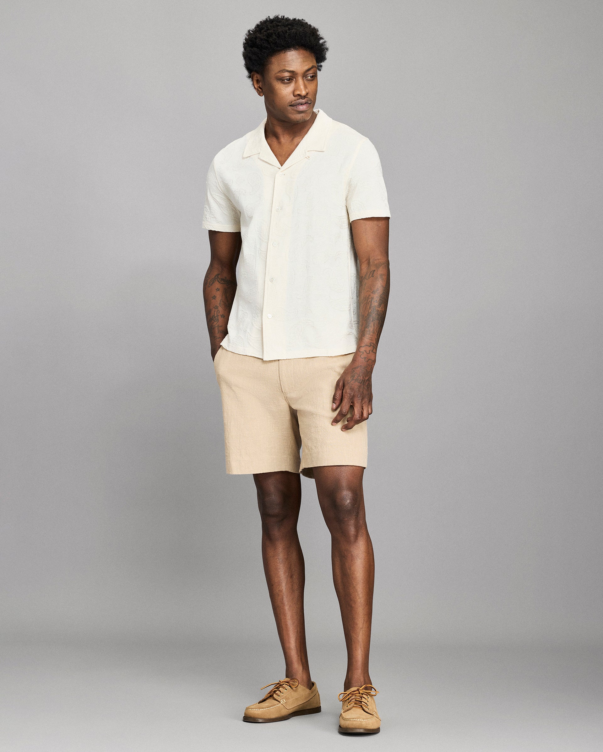 Man wearing a white shirt and beige shorts against a gray background