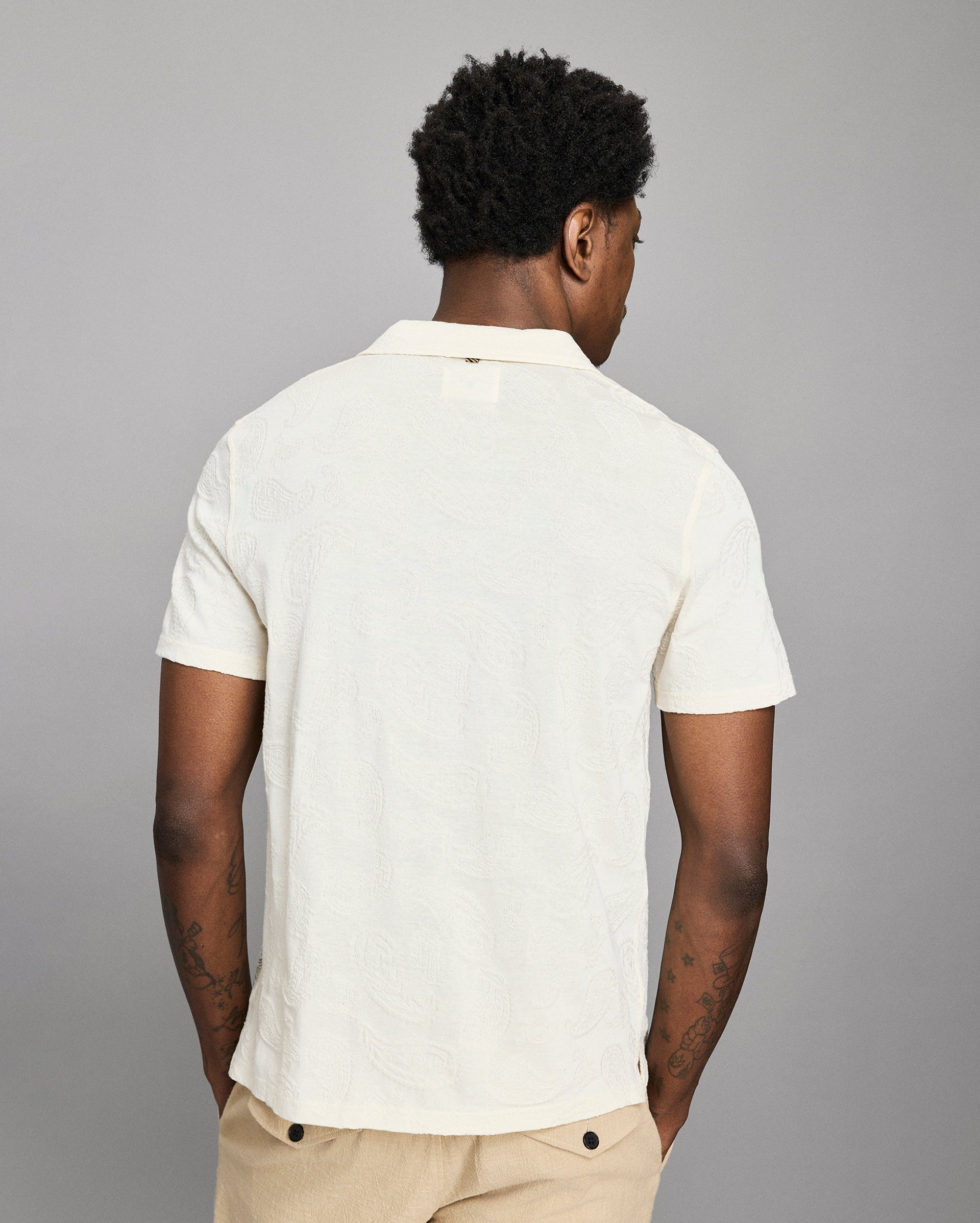 Person wearing a white polo shirt and beige pants against a gray background