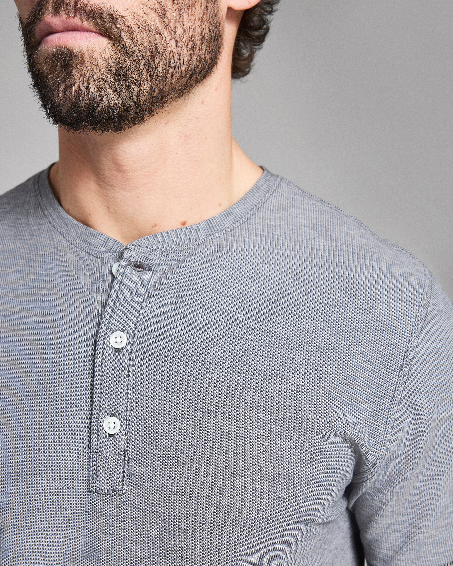 Close-up of a person wearing a gray henley shirt against a gray background