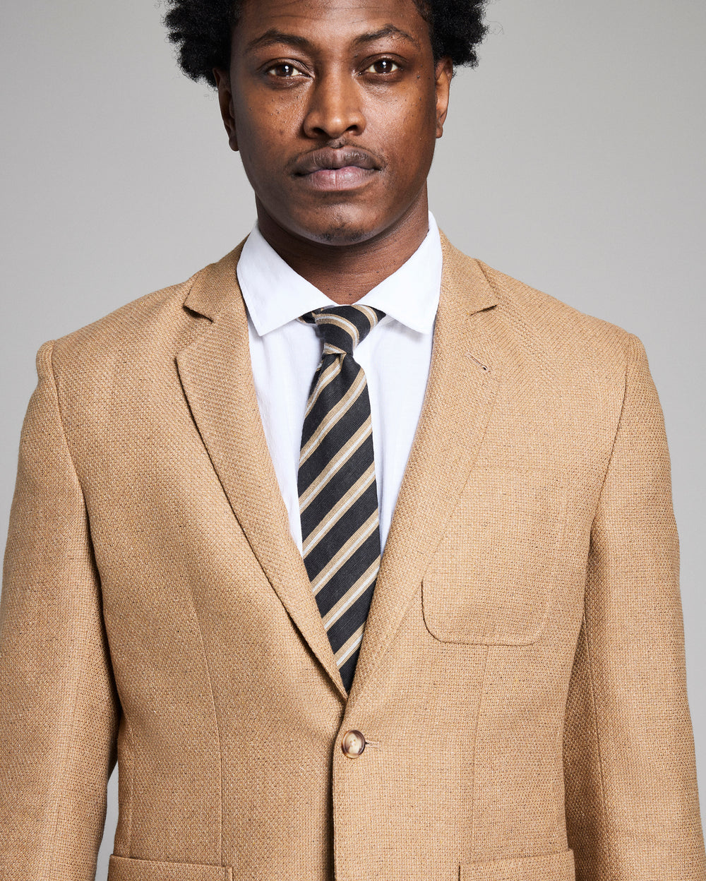 Man wearing a beige suit with a striped tie against a gray background