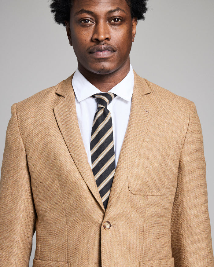 Man wearing a beige suit with a striped tie against a gray background