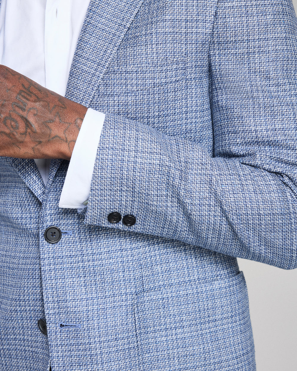 Close-up of a blue textured blazer with a white shirt and tattooed arm.