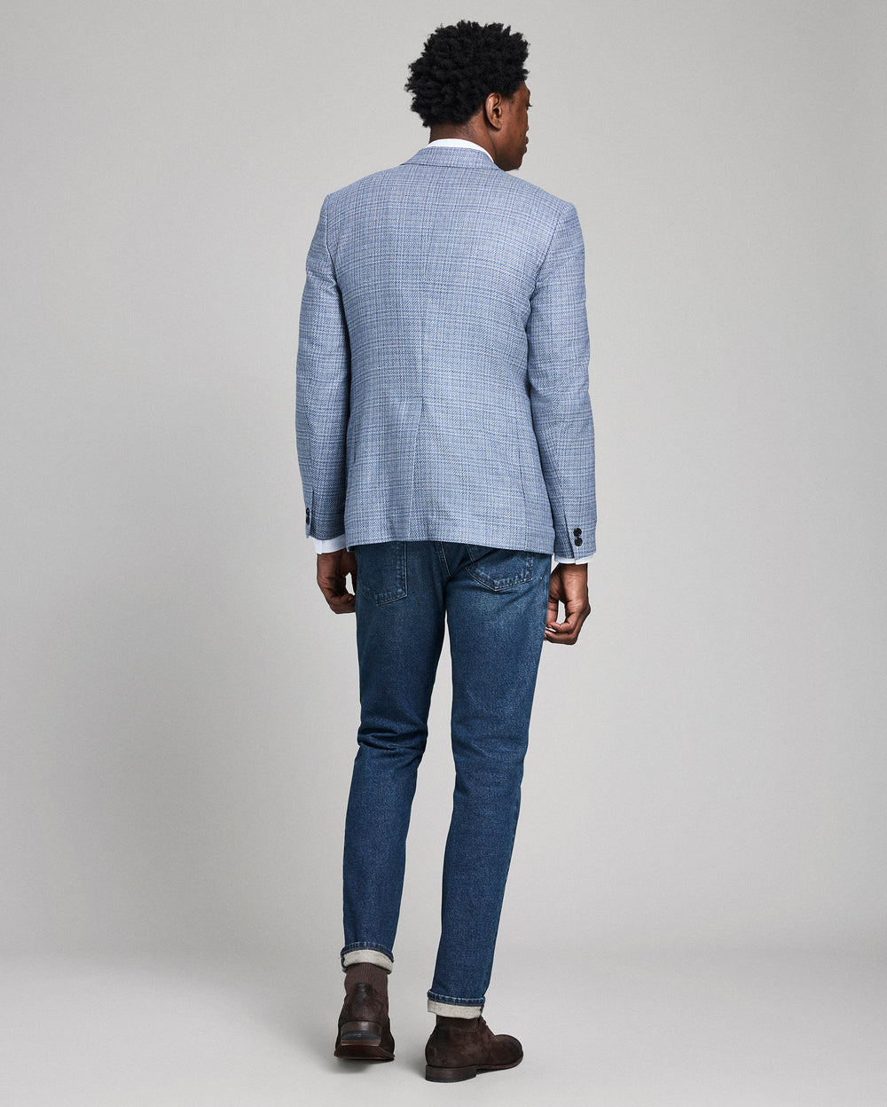 Person wearing a blue checkered blazer and jeans on a plain background