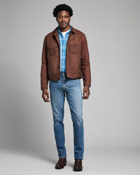 Man wearing a brown jacket, blue shirt, and jeans on a gray background