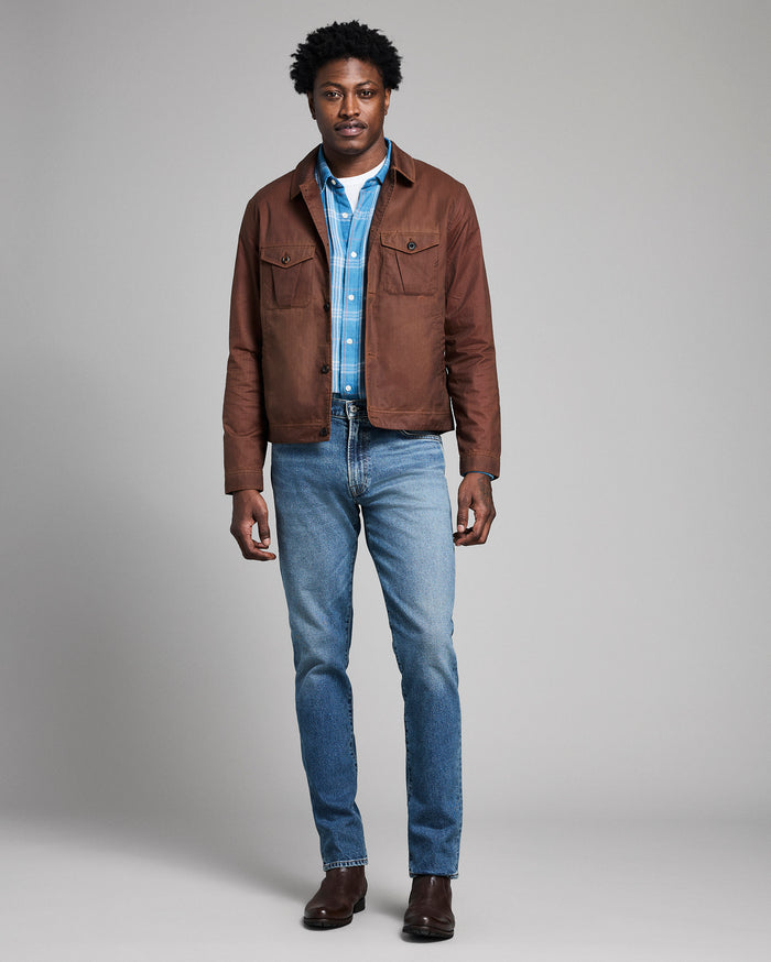 Man wearing a brown jacket, blue shirt, and jeans on a gray background