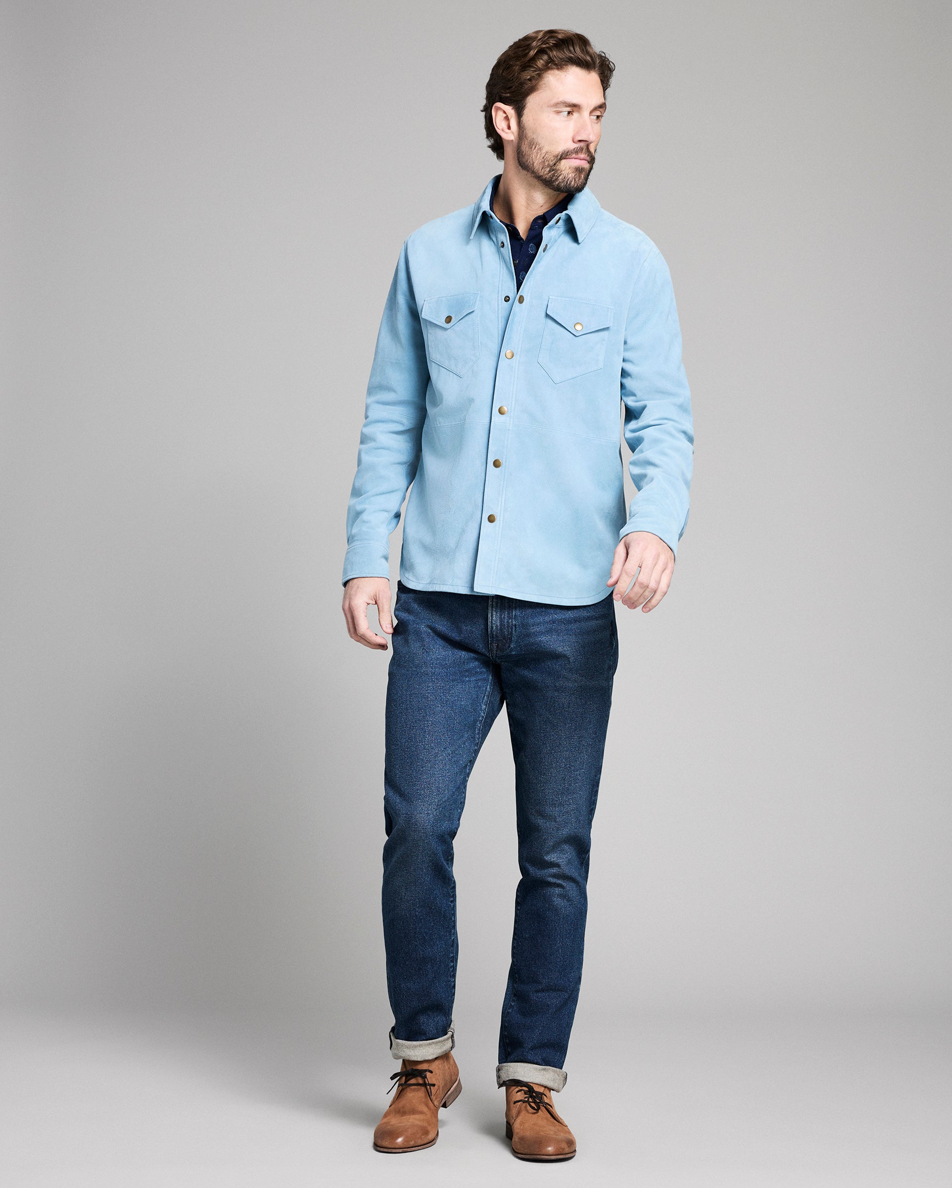 Man wearing a light blue denim jacket and dark blue jeans on a gray background