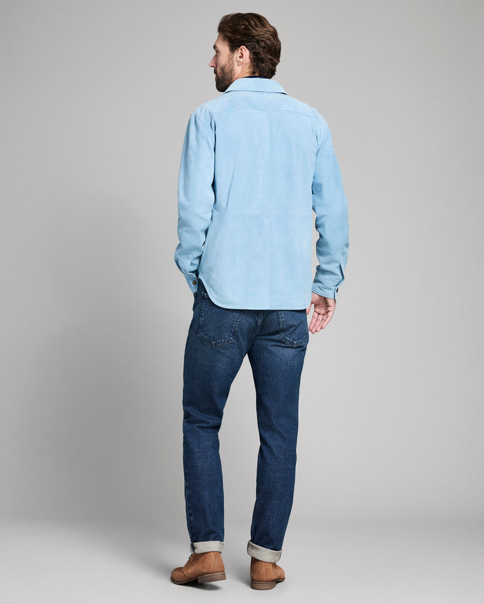 Man wearing a light blue shirt and dark blue jeans on a plain background