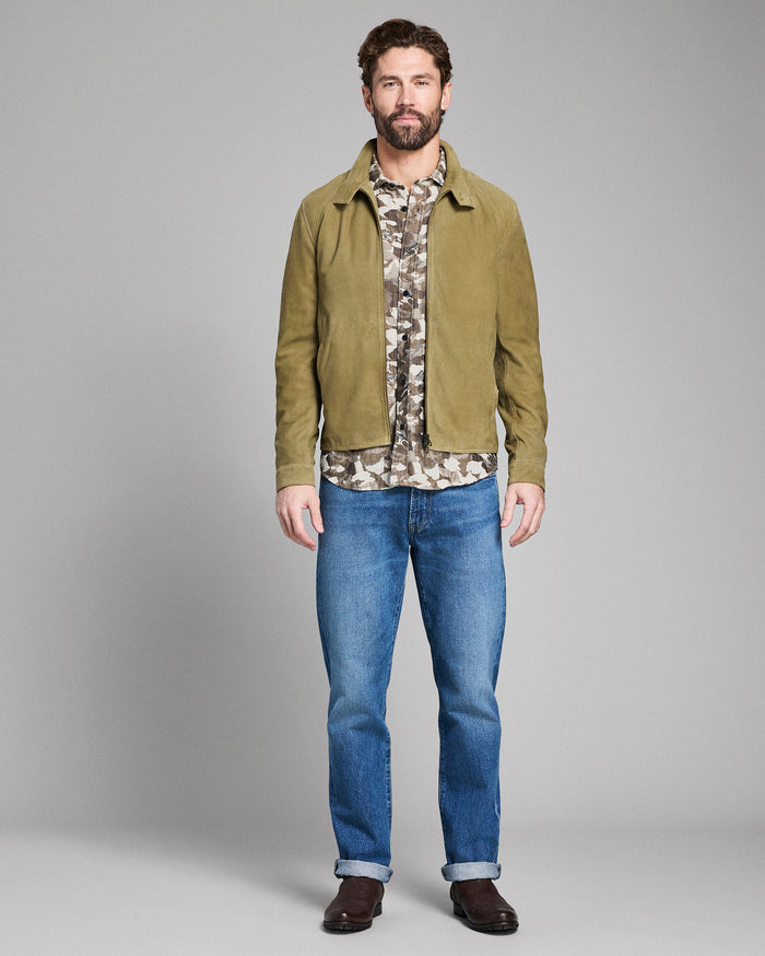 Man wearing a green jacket, camouflage shirt, and blue jeans on a gray background