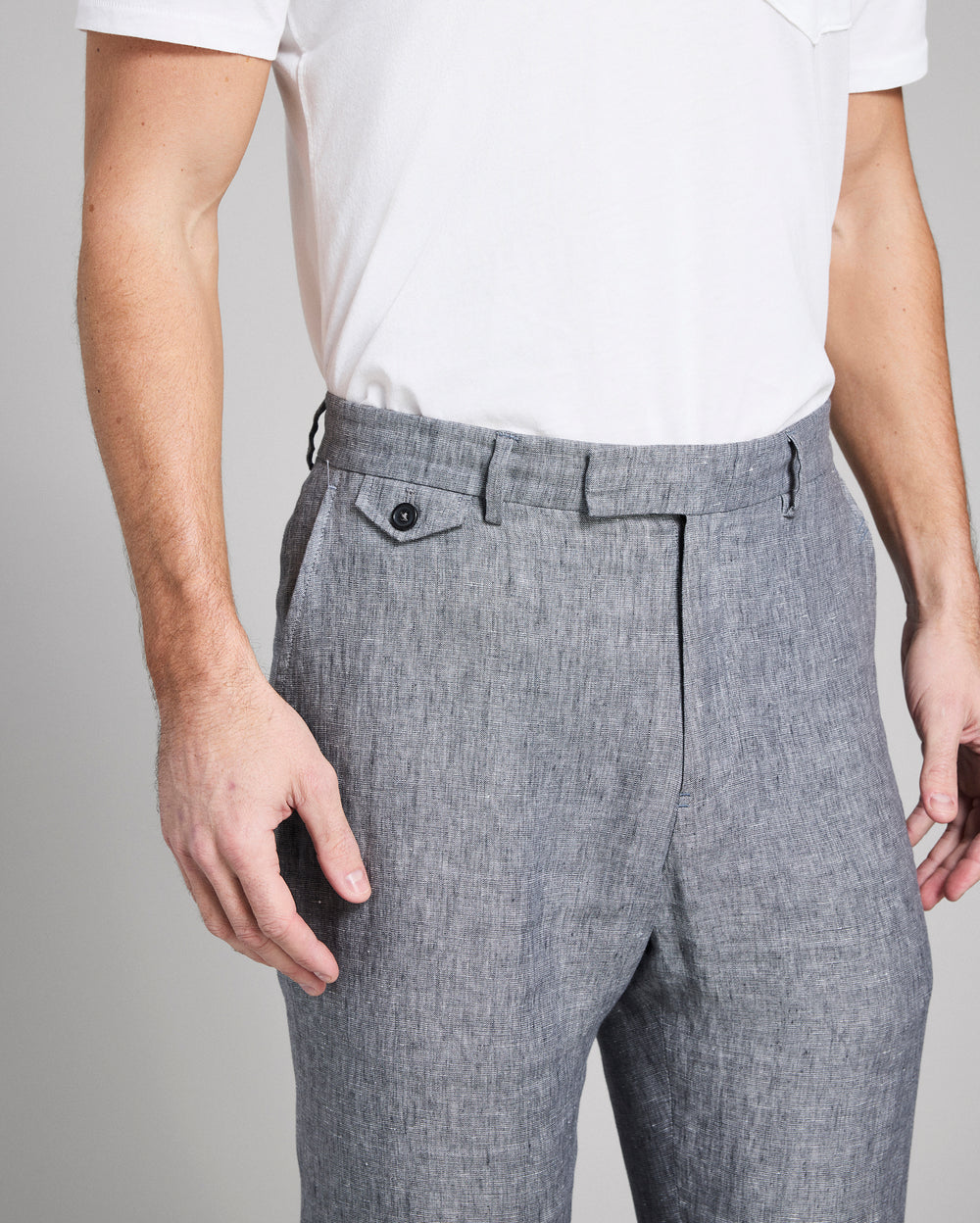 Person wearing gray pleated pants and a white shirt on a plain background