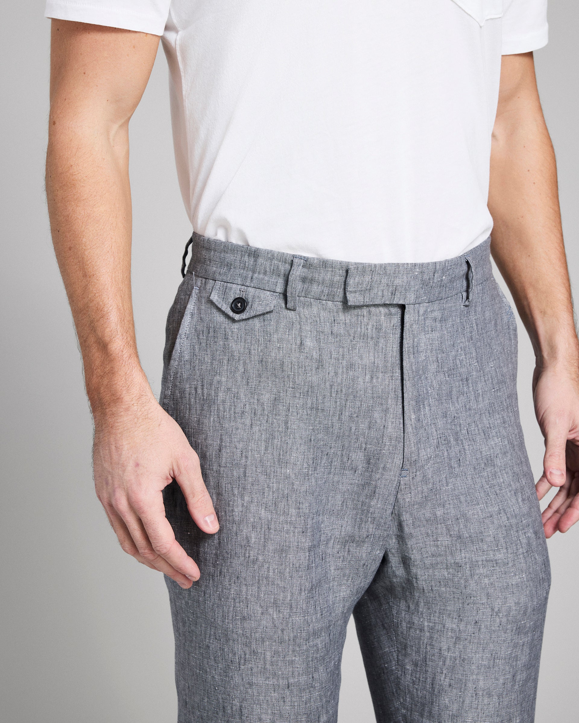 Person wearing gray pleated pants and a white shirt on a plain background