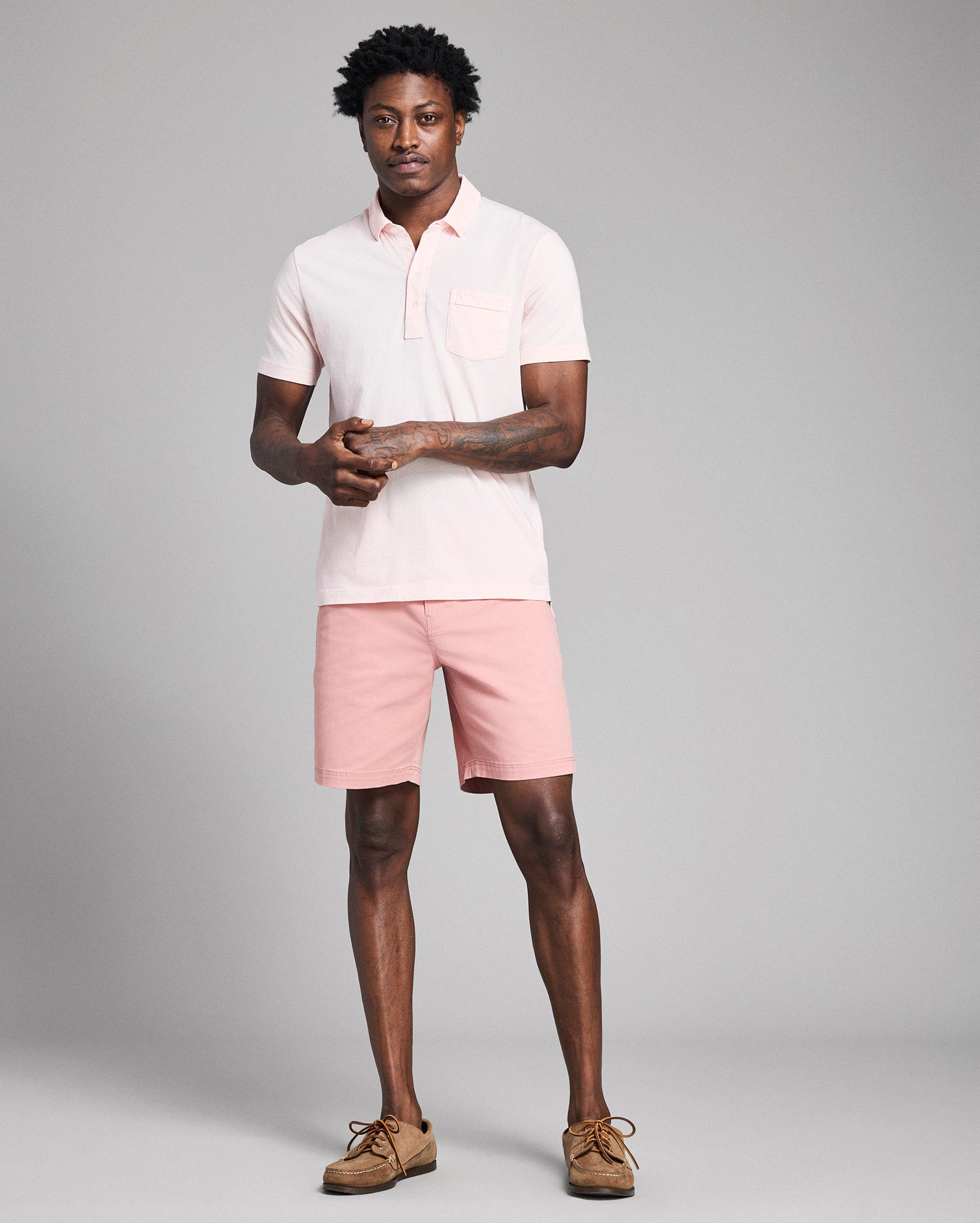 Man wearing a light pink polo shirt and shorts on a gray background