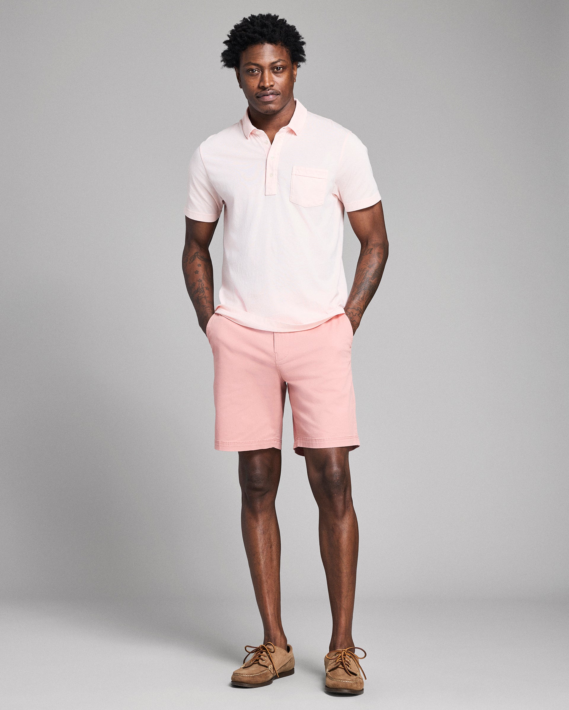 Man wearing a light pink polo shirt and shorts on a gray background