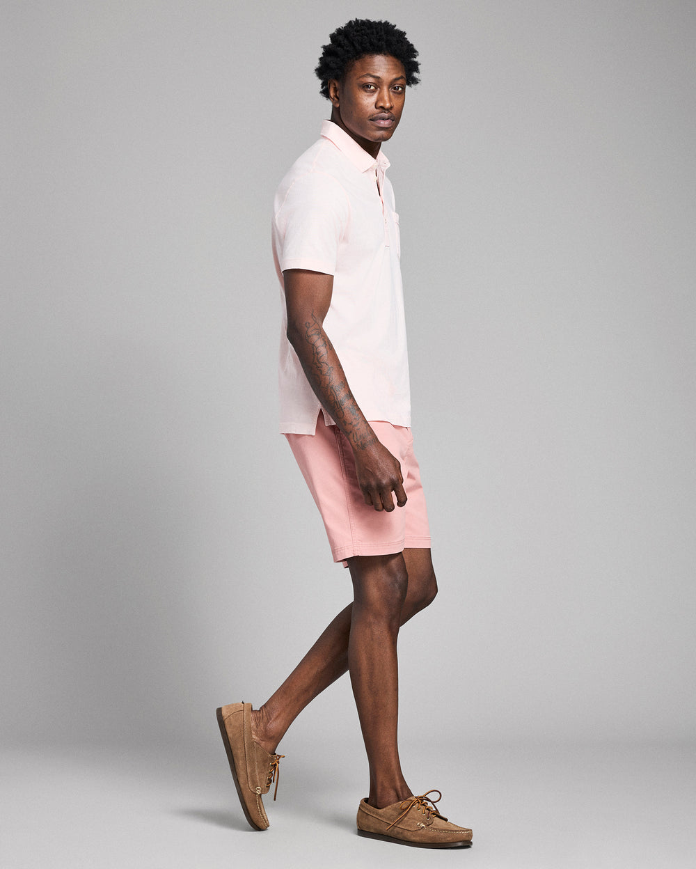 Person wearing a white polo shirt and pink shorts on a gray background