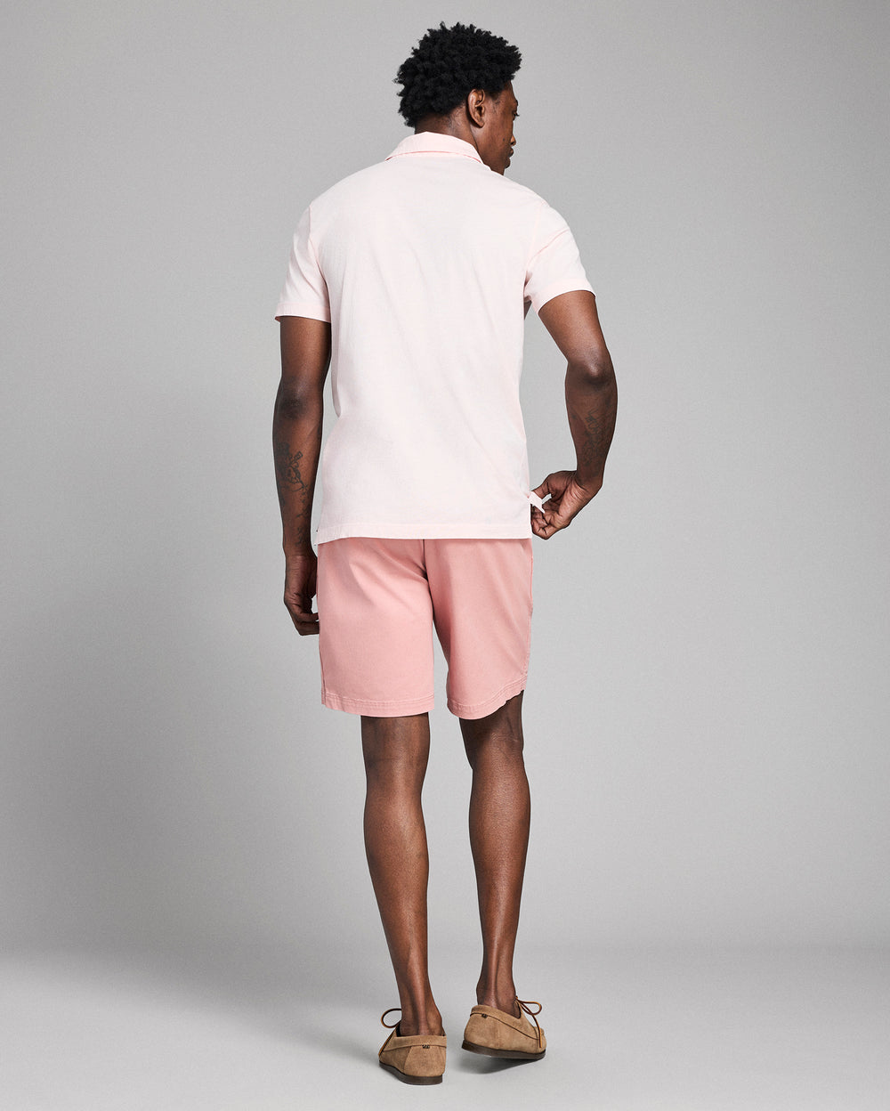 Man wearing a white polo shirt and pink shorts on a gray background