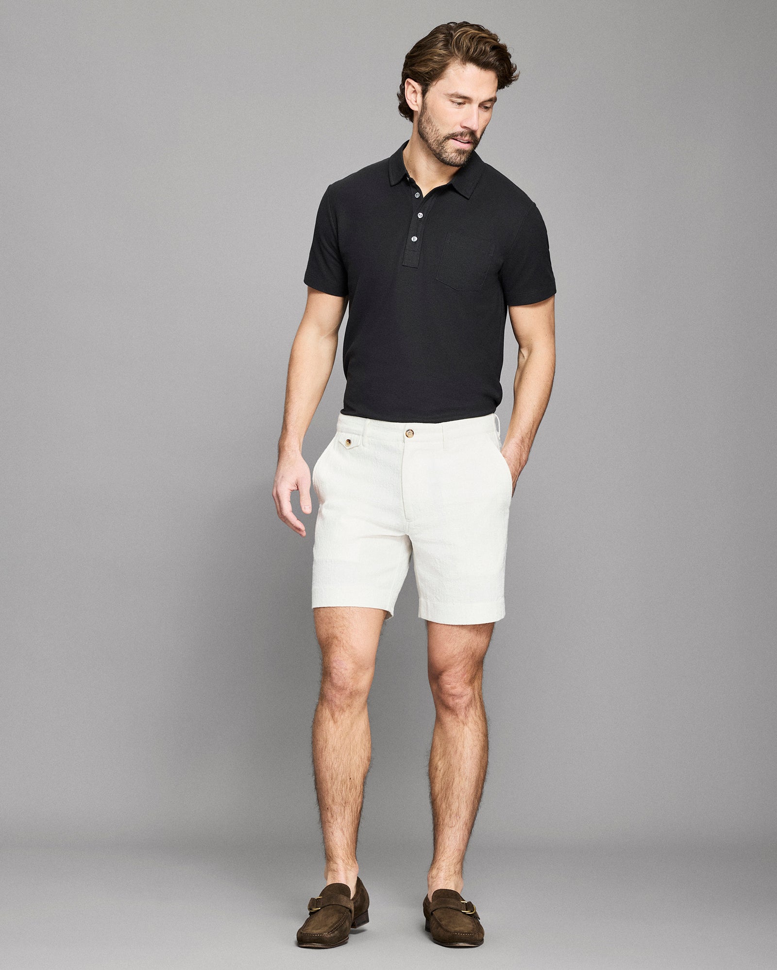 Man wearing a black polo shirt and white shorts against a gray background