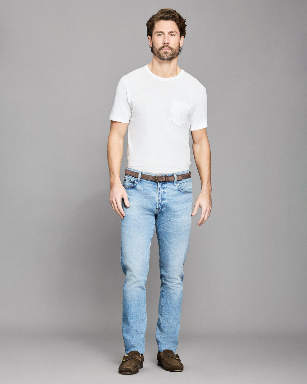 Man wearing a white t-shirt and light blue jeans on a gray background