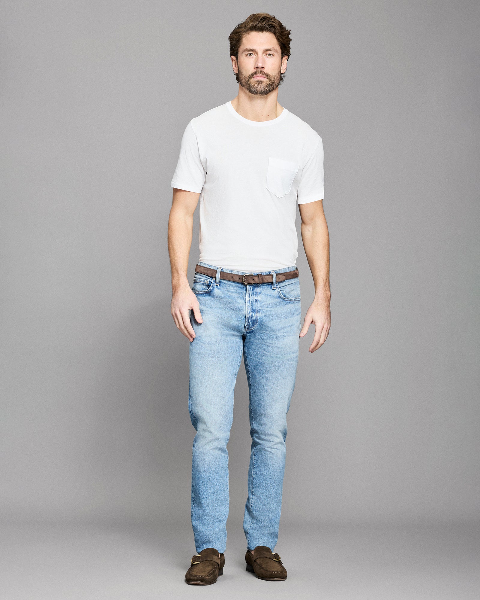 Man wearing a white t-shirt and light blue jeans on a gray background