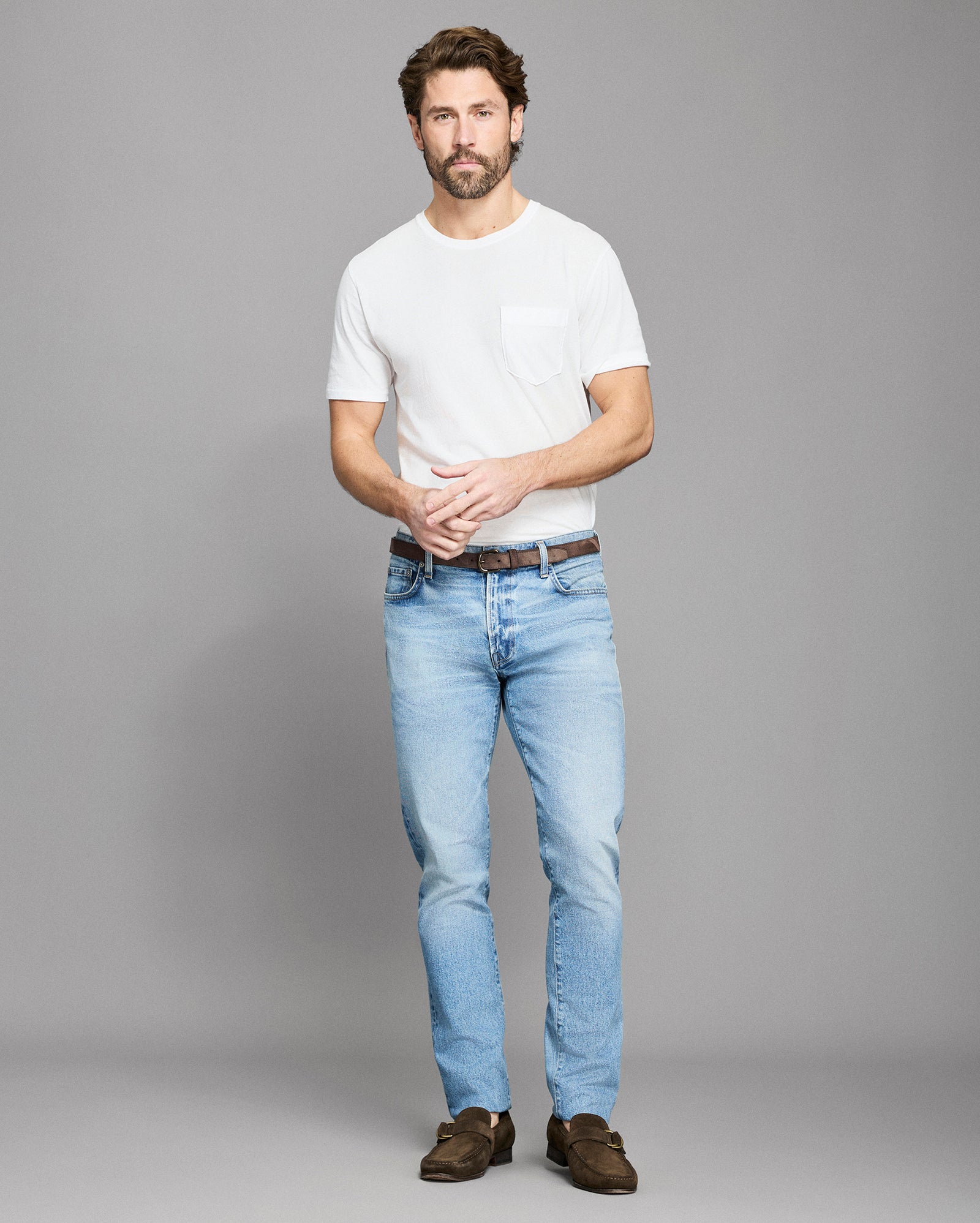 Man wearing a white t-shirt and light blue jeans against a gray background
