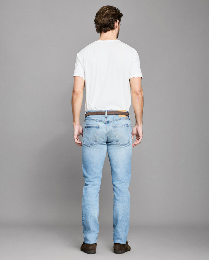 Man wearing light blue jeans and a white t-shirt on a gray background