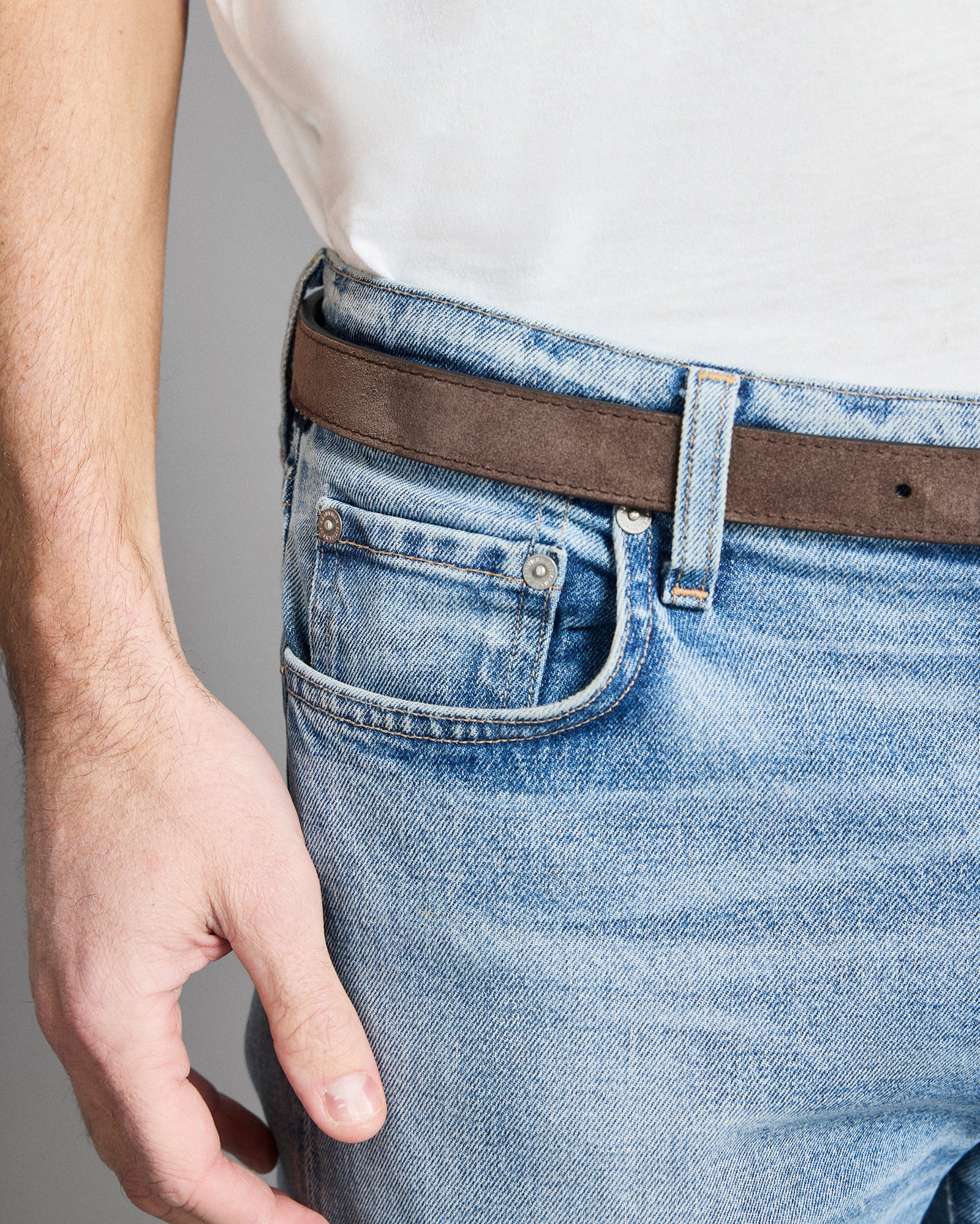 Close-up of a person wearing blue jeans with a brown belt on a gray background