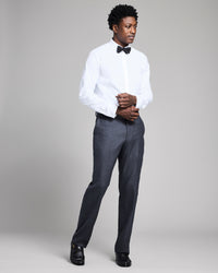 Man wearing a white dress shirt, black bow tie, gray pants, and black shoes on a plain background