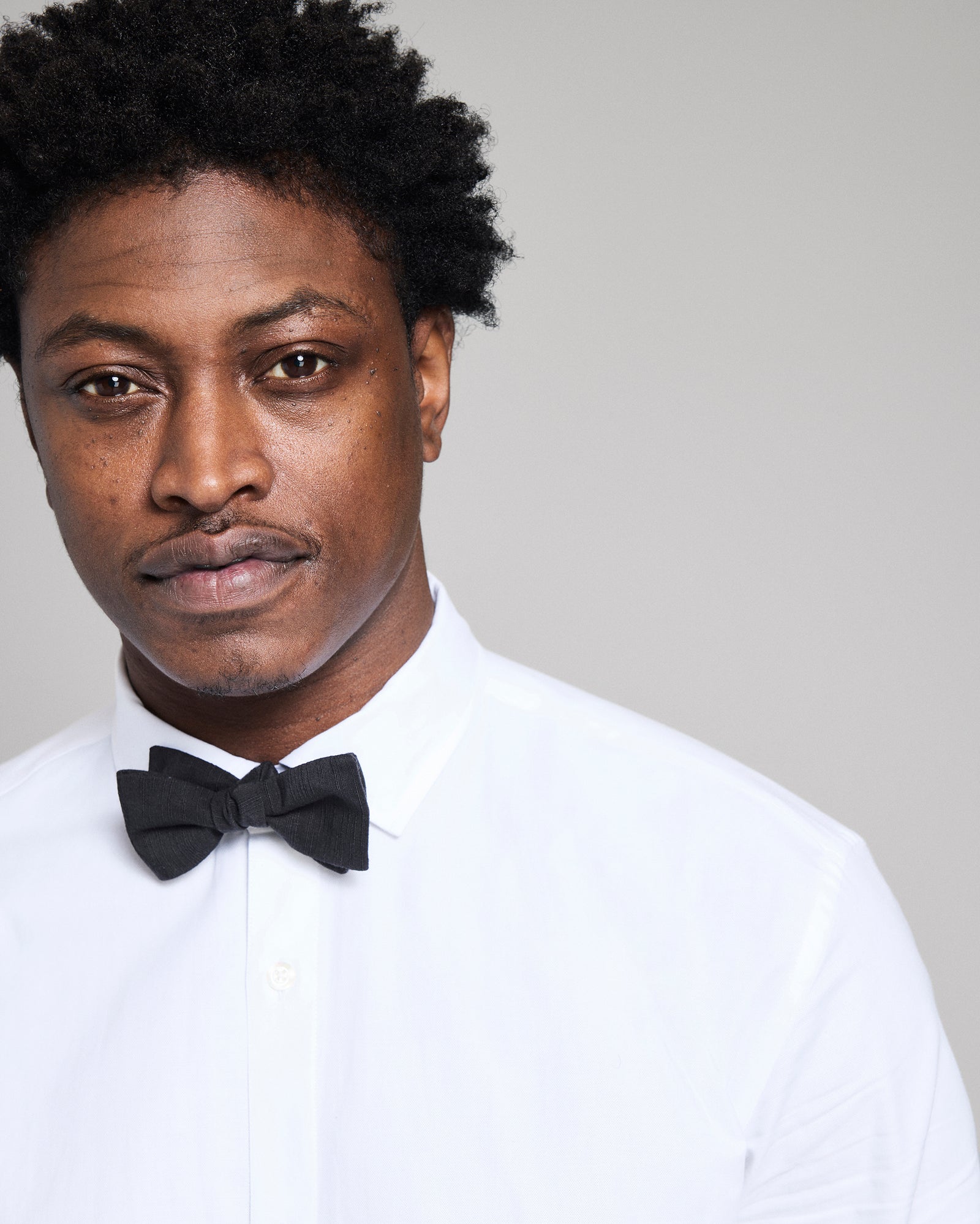 Man wearing a white shirt and black bow tie against a plain background