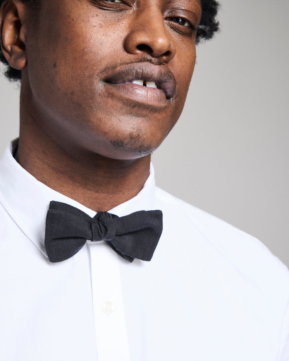 Man wearing a black bow tie and white shirt against a neutral background