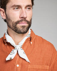Man wearing an orange shirt with a white scarf around his neck against a gray background
