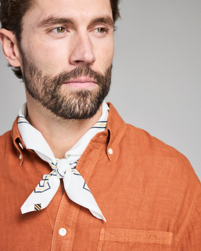 Man wearing an orange shirt with a white scarf around his neck against a gray background