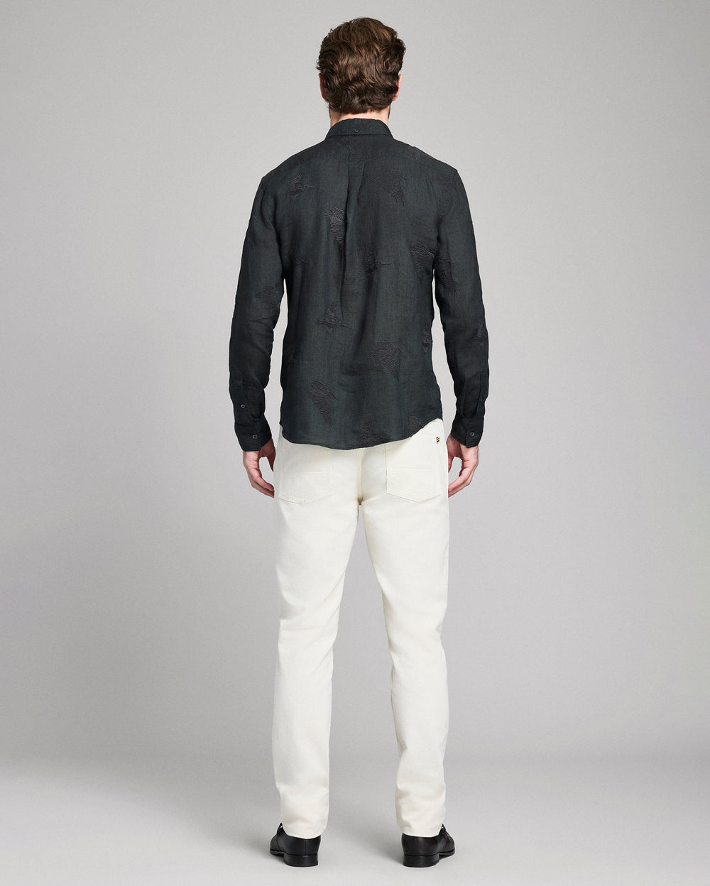 Man wearing a black shirt and white pants on a gray background