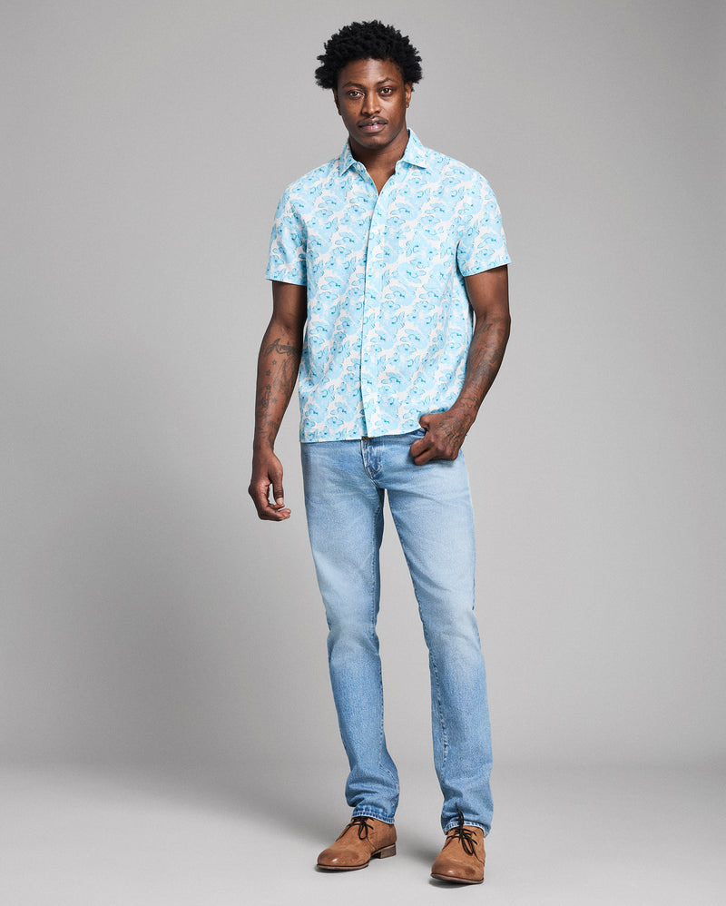 Man wearing a light blue patterned shirt and jeans on a gray background Alternate