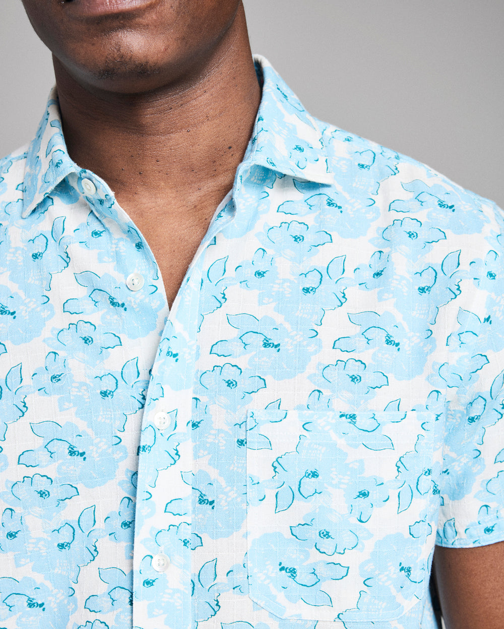 Close-up of a person wearing a light blue floral patterned shirt against a neutral background