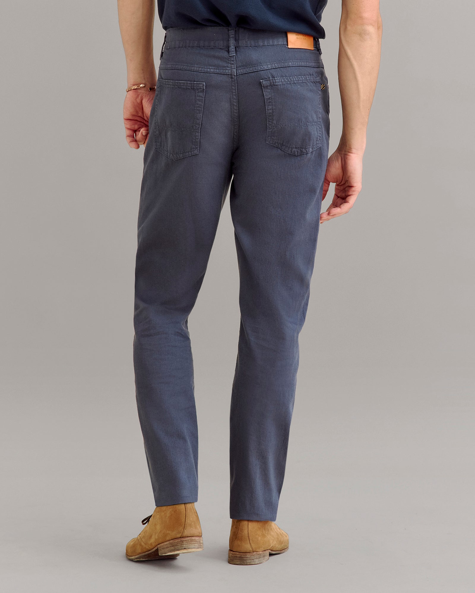 A person wearing dark blue pants, brown shoes, and a navy shirt is shown from the back, standing on a light gray background.