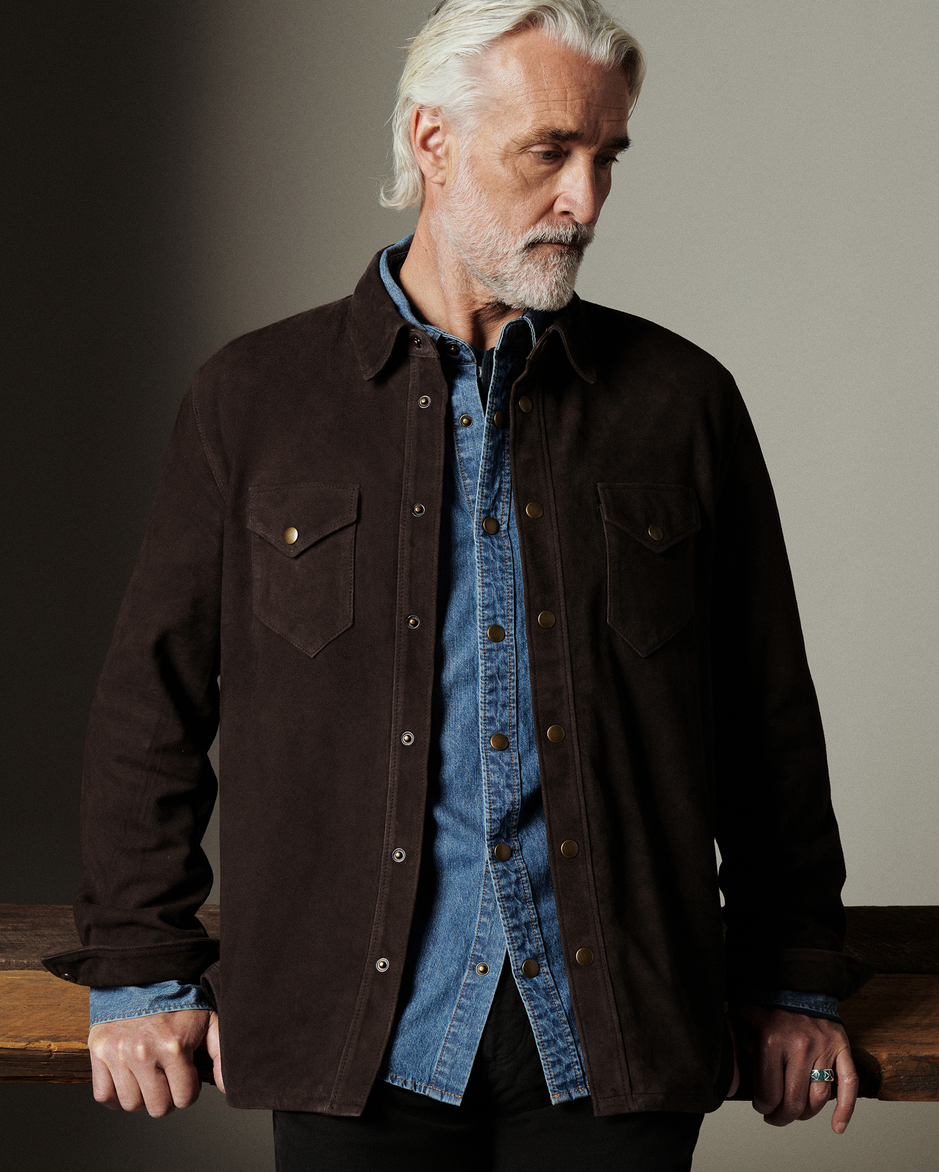 Man wearing a dark brown jacket over a blue shirt against a neutral background