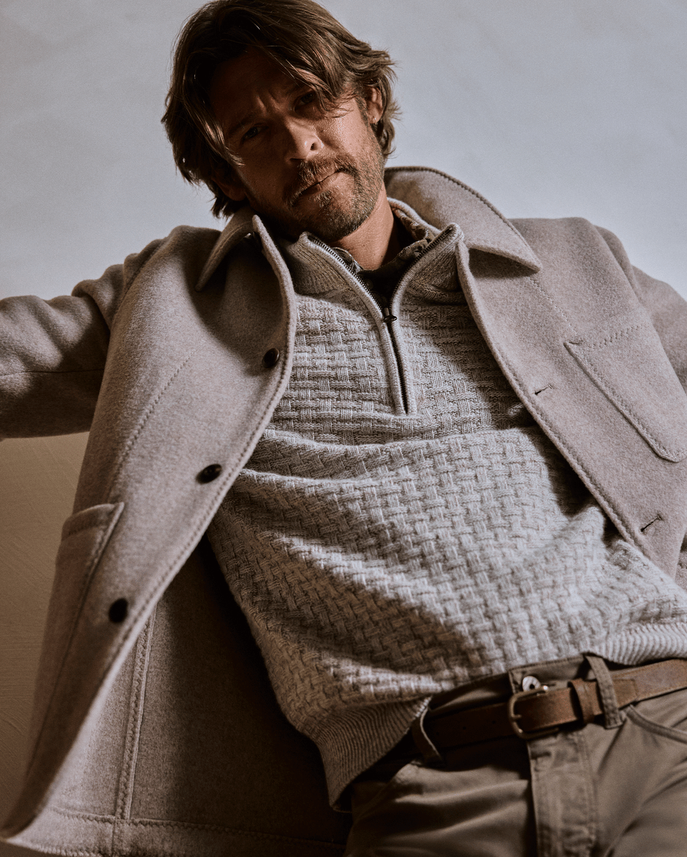 Man wearing a beige coat over a textured sweater against a neutral background