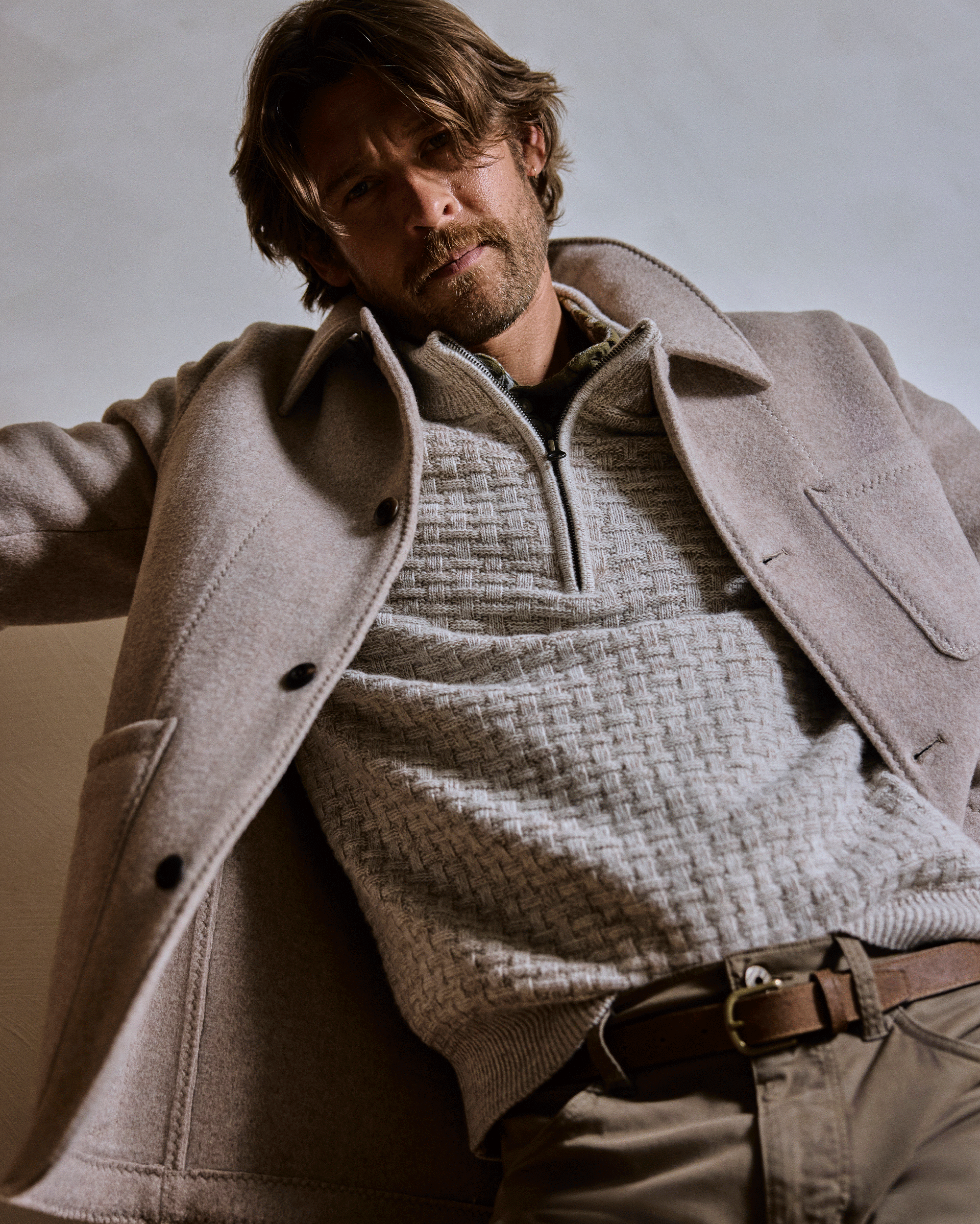 Man wearing a beige coat over a textured sweater against a neutral background