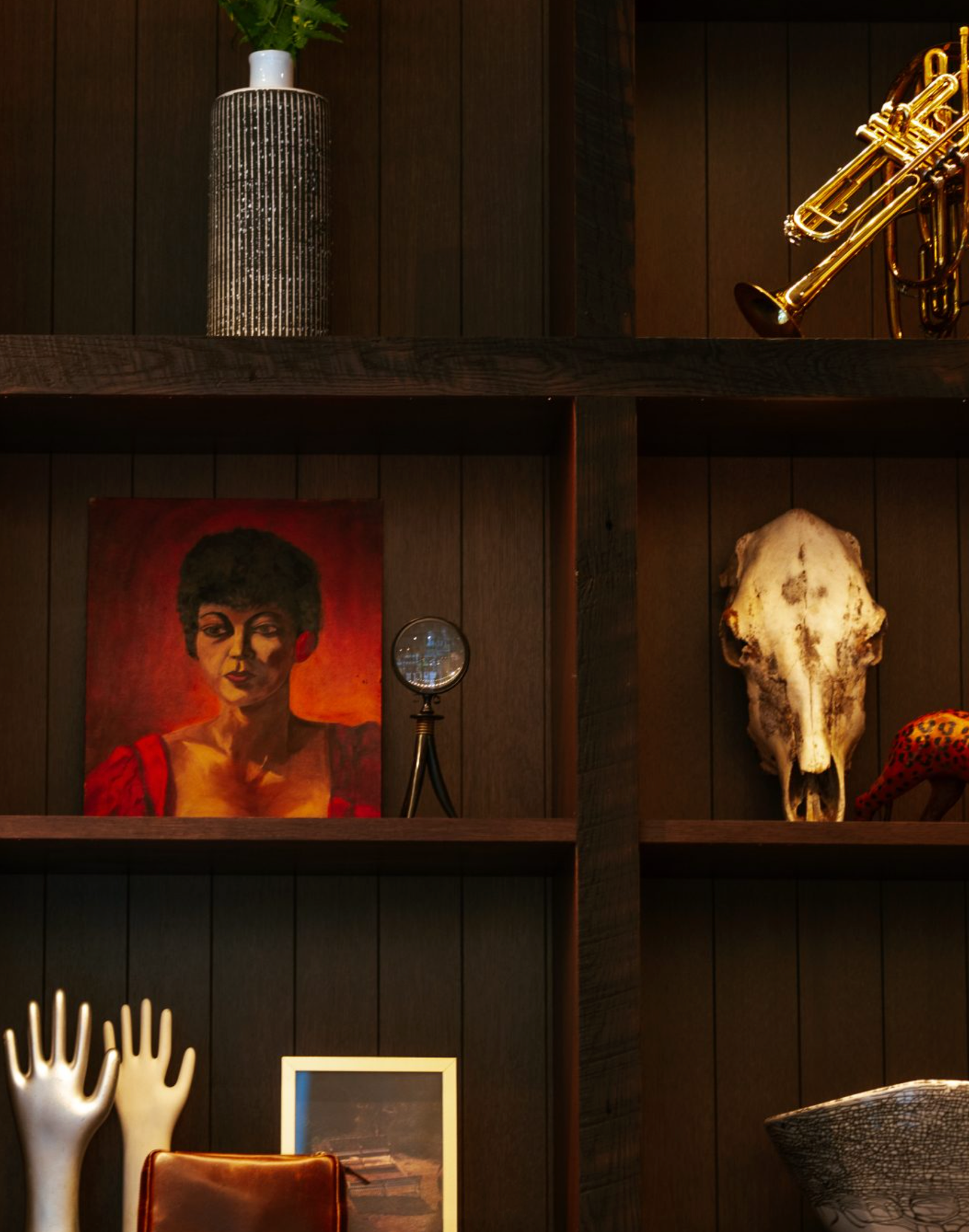 Decorative shelf with various items including a portrait, skull, and musical instrument against a wooden wall.