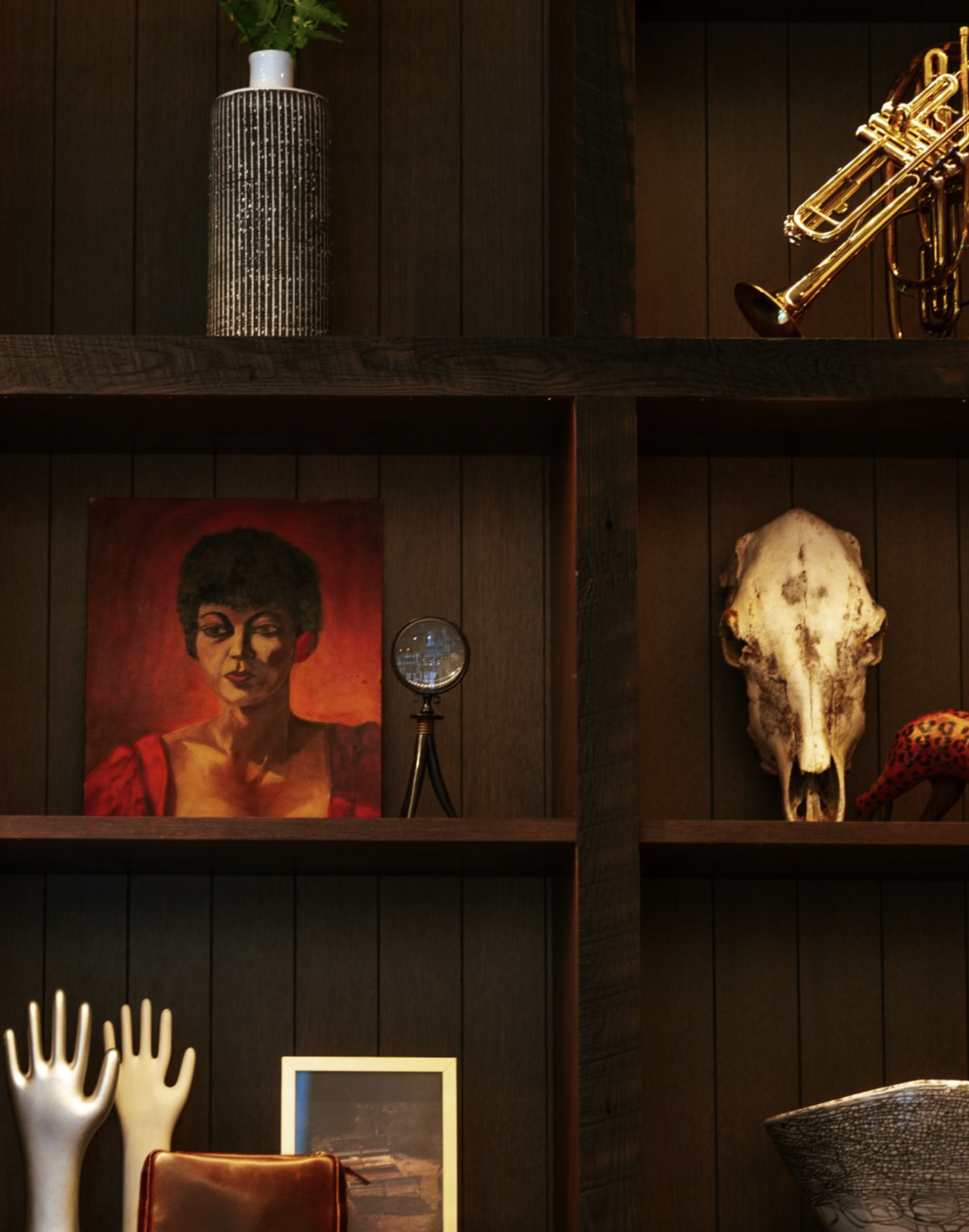 Decorative shelf with various items including a portrait, skull, and musical instrument against a wooden wall.