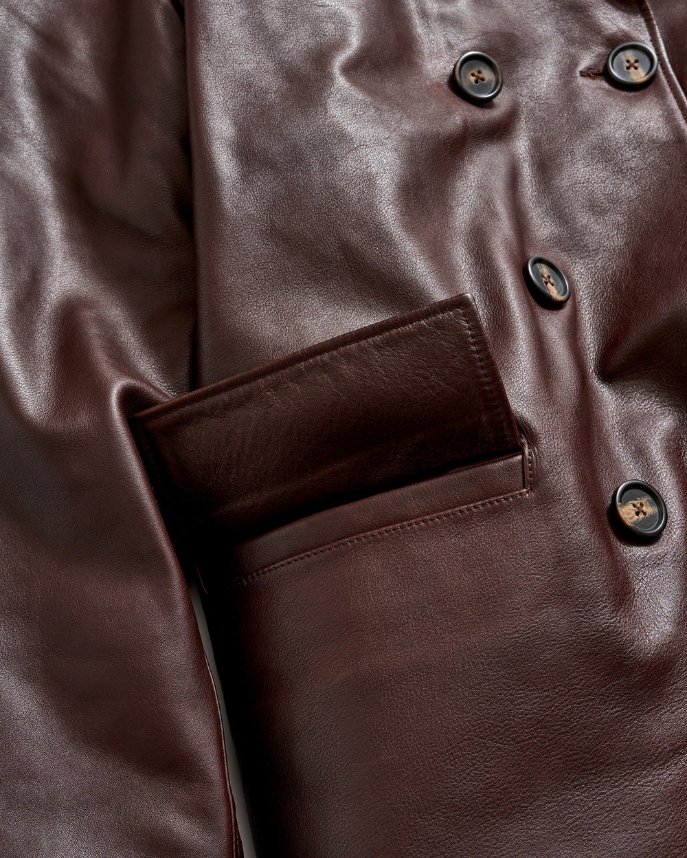 Close-up of a brown leather jacket featuring black buttons and a front pocket, highlighting the smooth texture and sheen of the material.