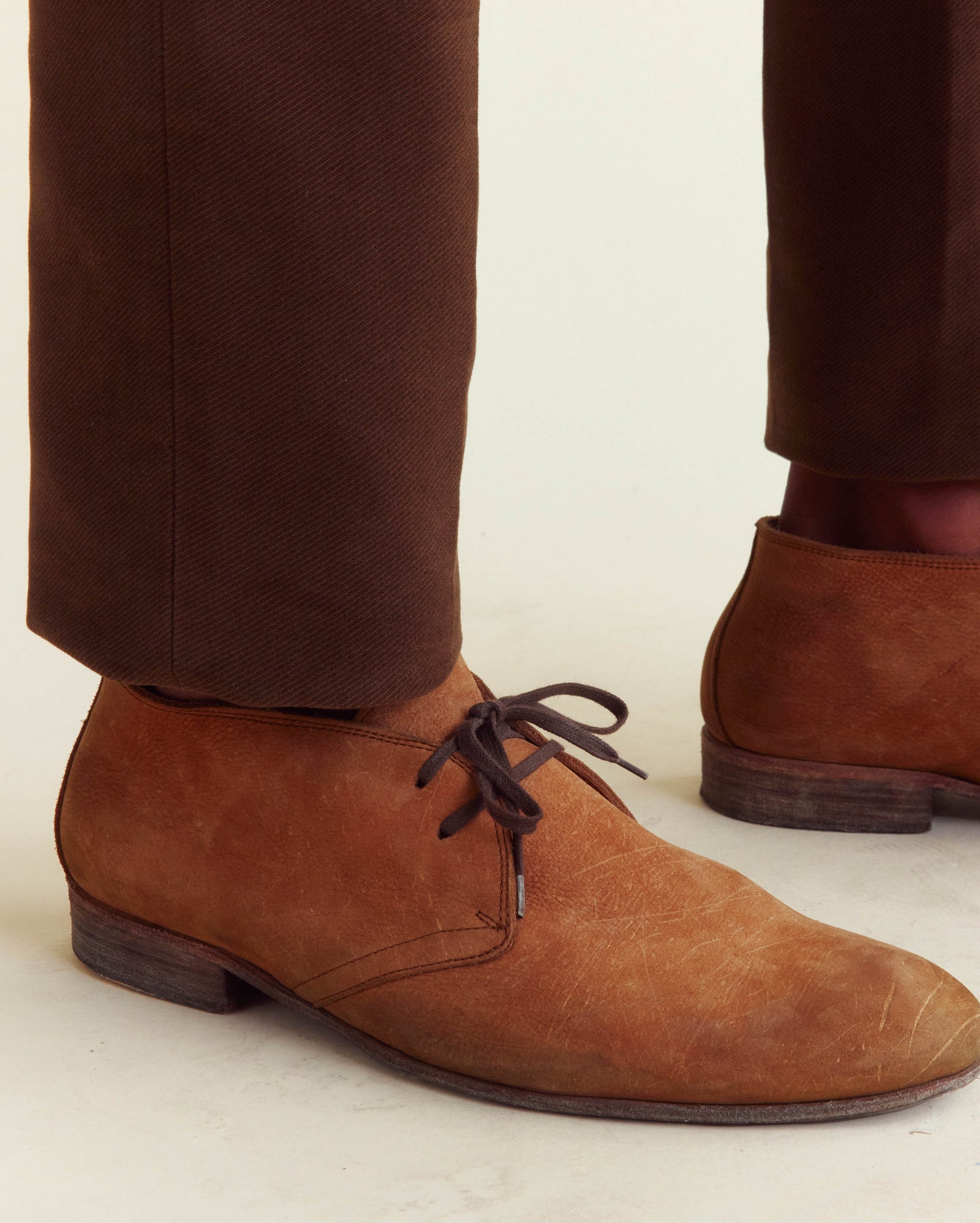 Brown suede shoes worn with brown pants on a light background