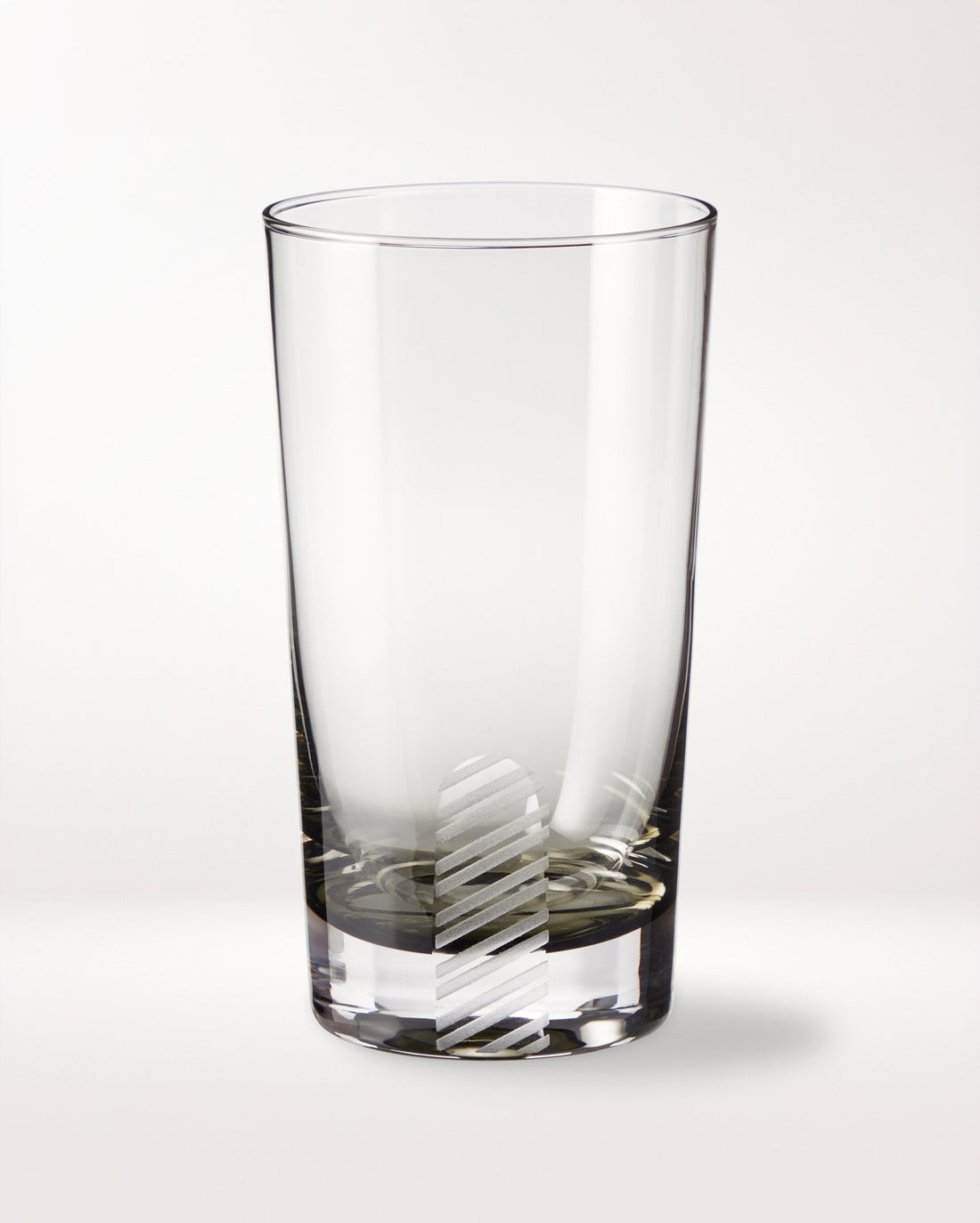 A clear empty glass tumbler with a vertical, diagonal-striped frosted pattern near the base, placed on a plain white background.