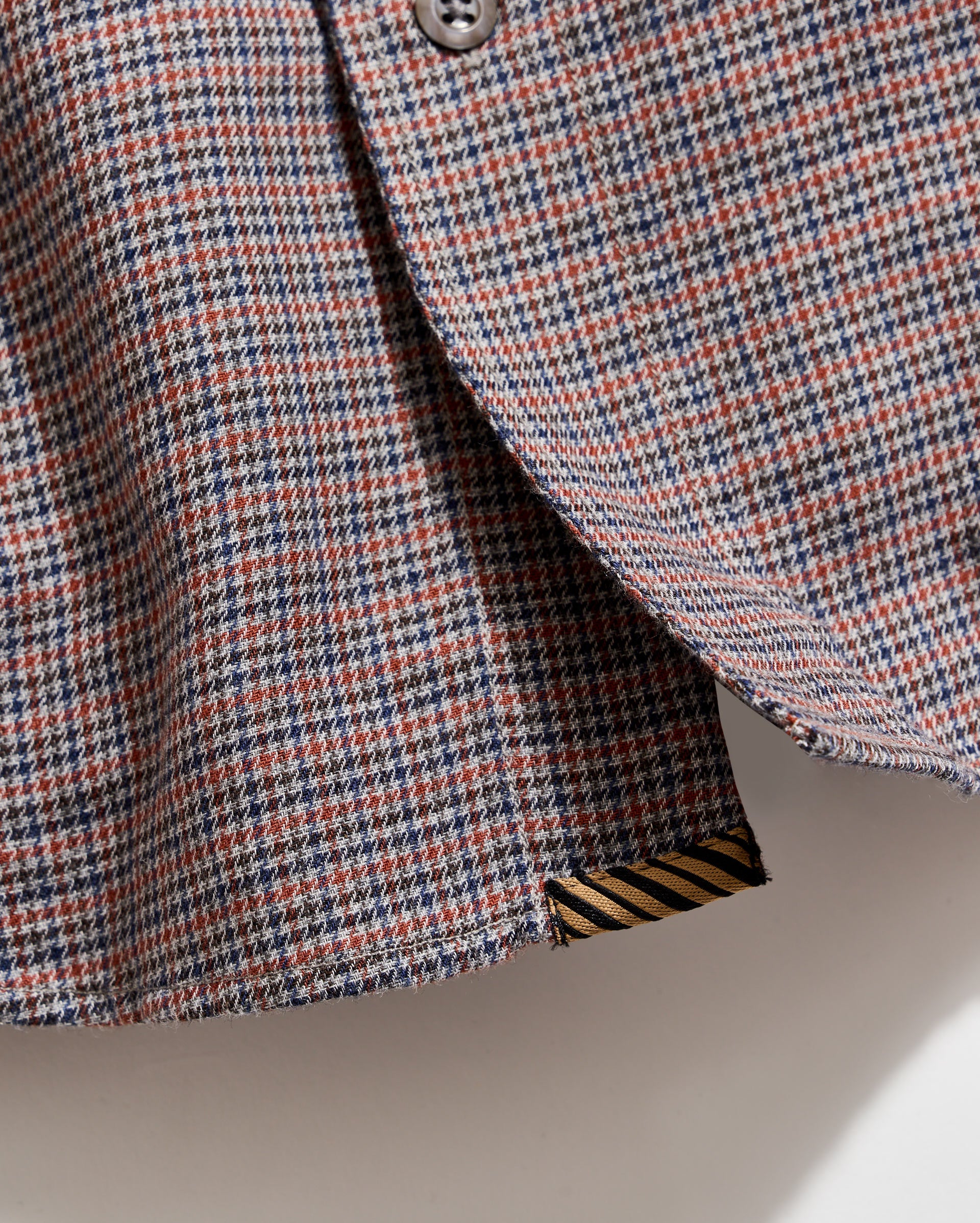 Close-up of a houndstooth patterned fabric with a button on a neutral background