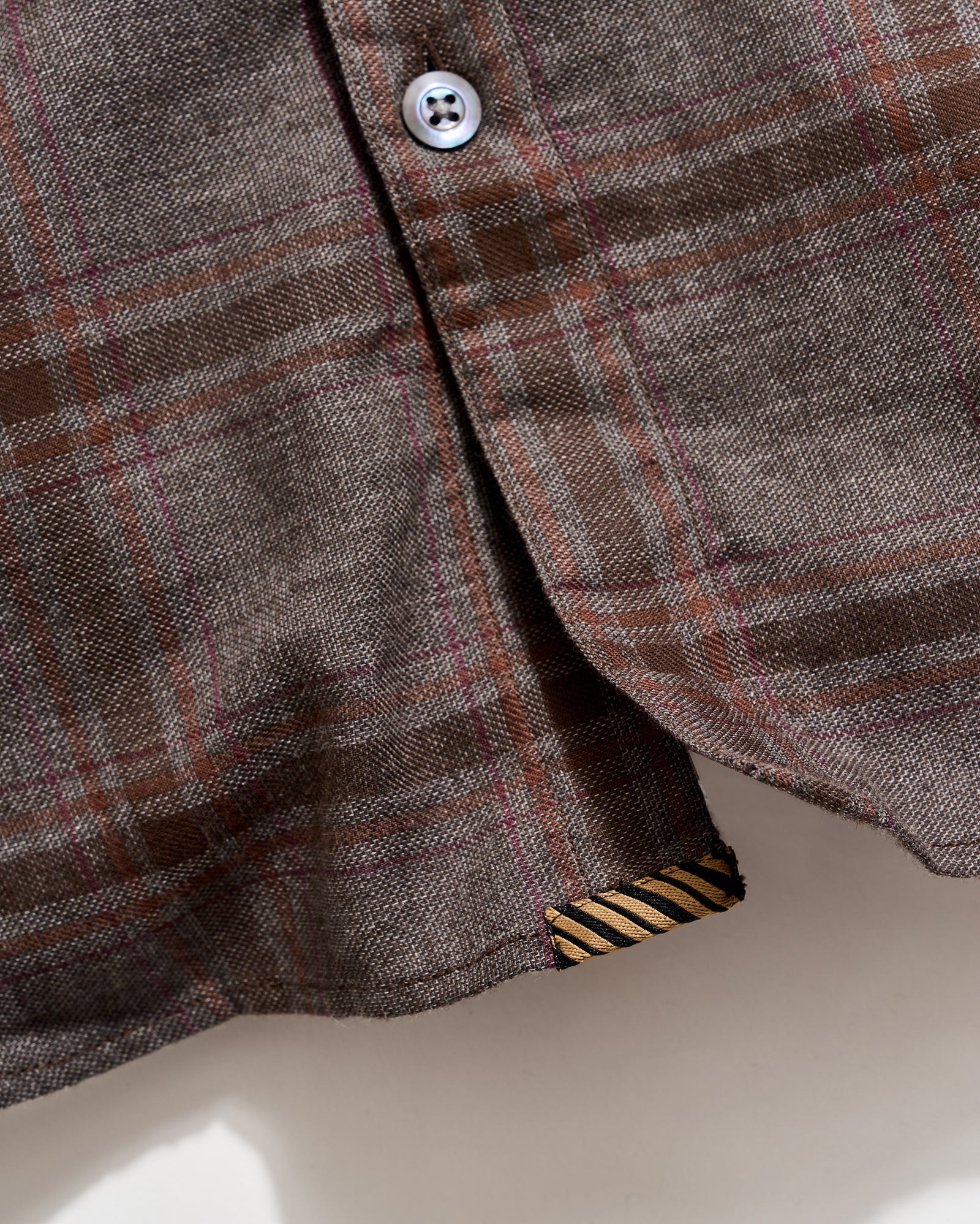 Close-up of a plaid shirt with a button and collar detail on a neutral background