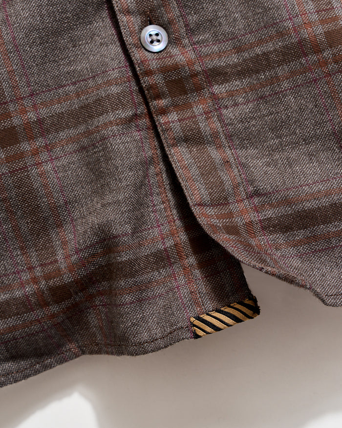 Close-up of a plaid shirt with a button and collar detail on a neutral background