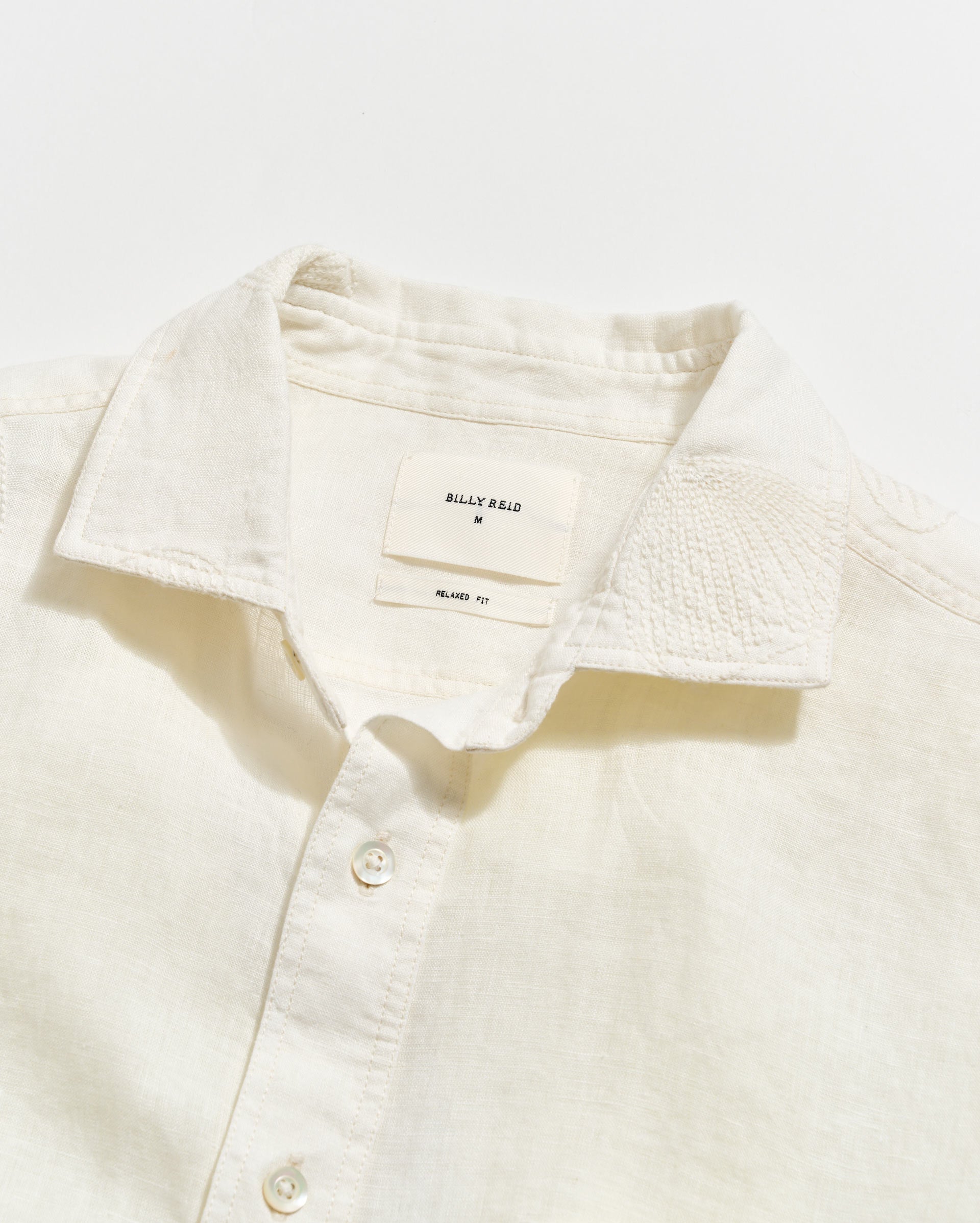 Close-up of a cream-colored shirt with a collar and buttons, featuring the brand 'Bally' on a white background.