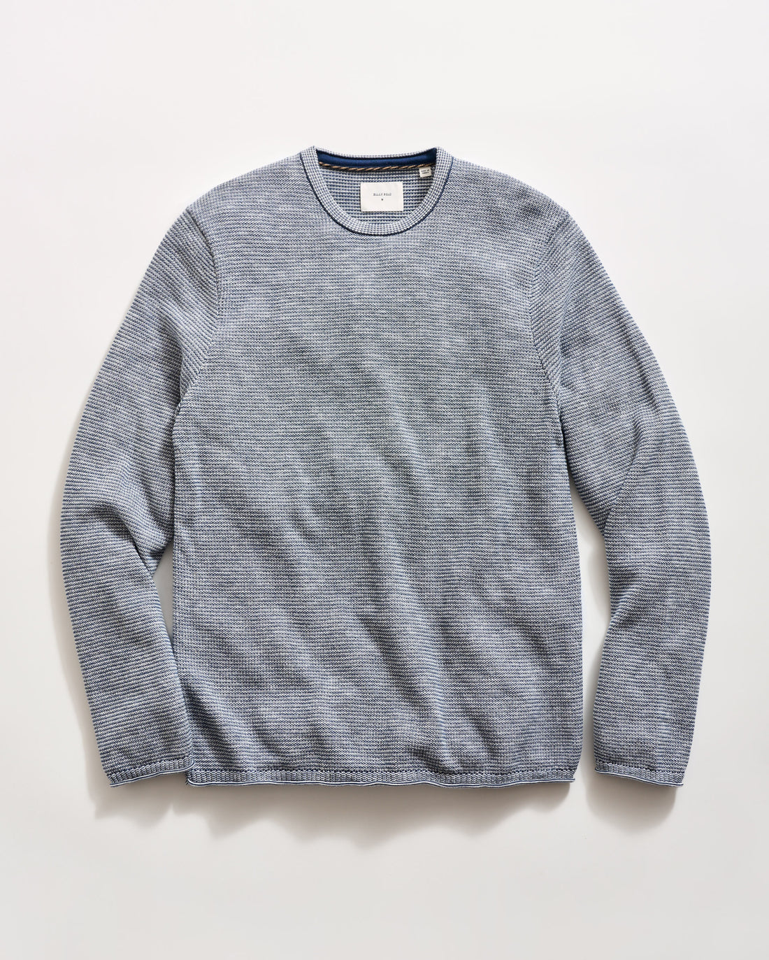 A blue striped long-sleeve crewneck knit sweater laid flat against a light off-white background.