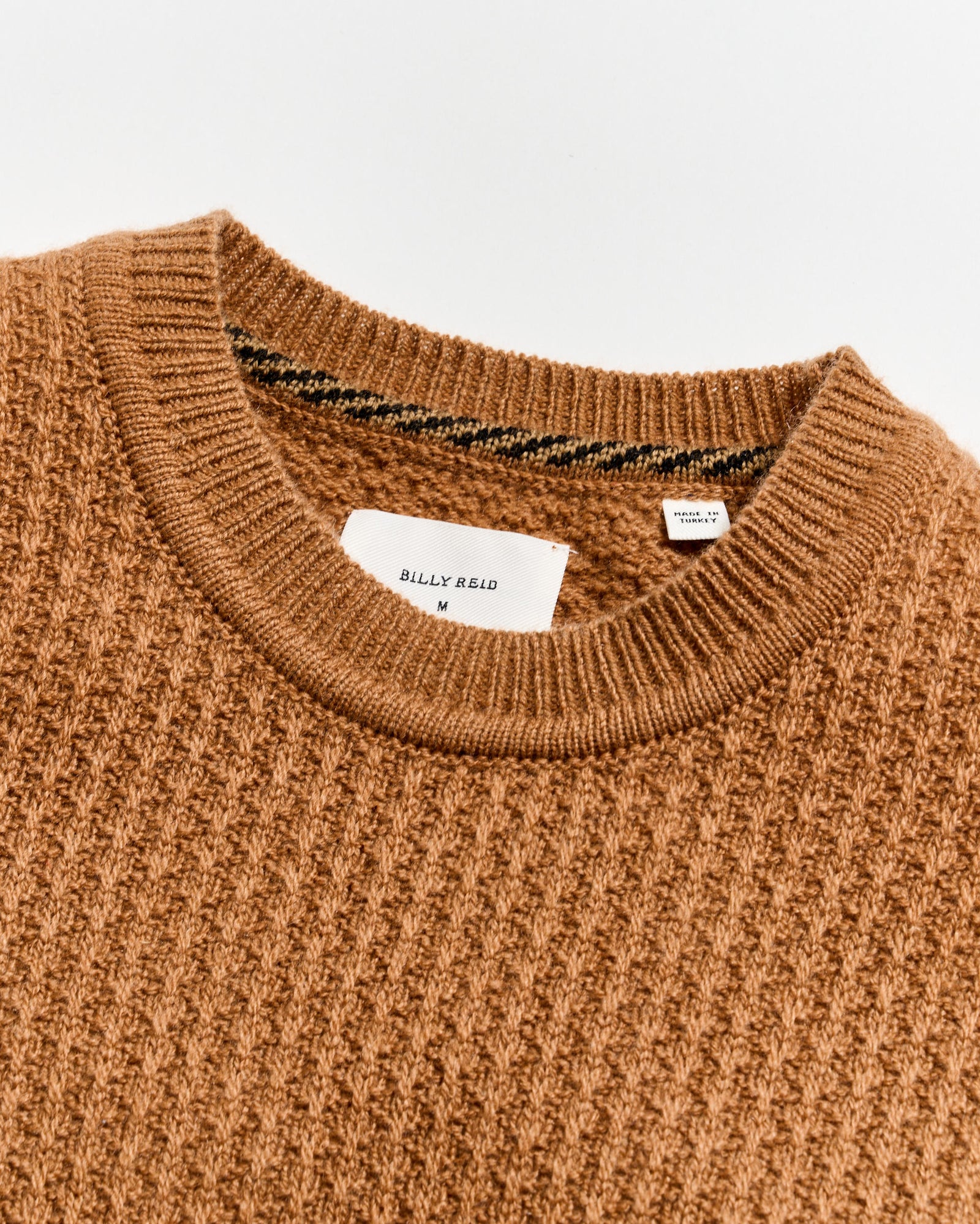 Close-up of a brown sweater with a brand label on a light gray background