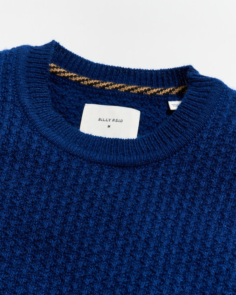 Close-up of a blue sweater with a brand label on a white background Alternate